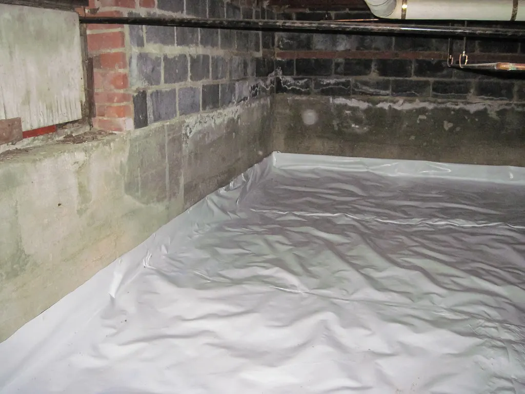 White vapor barrier covering the ground in a crawl space